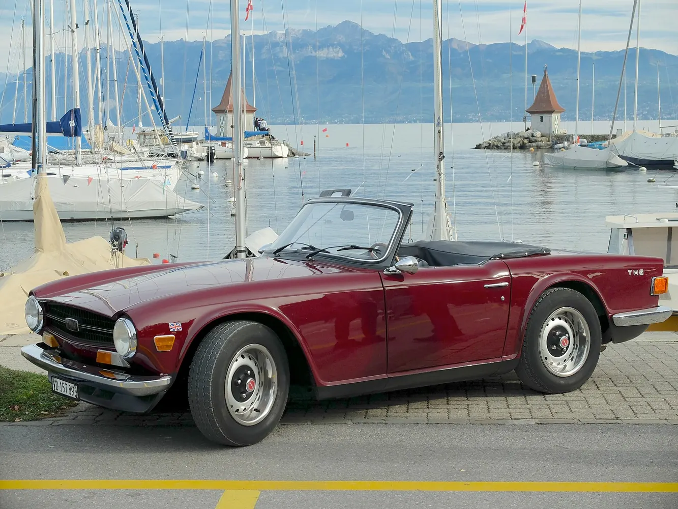 A burgundy Triumph TR6 roadster parked by a harbour